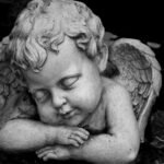 Close-up of a serene angel statue with closed eyes in grayscale, exuding peacefulness.