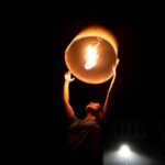 A person launches an illuminated sky lantern against a dark night sky, creating a warm glow.